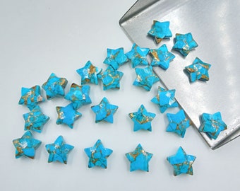 May include: A collection of turquoise star-shaped cabochons with gold accents. The cabochons are scattered on a silver surface.