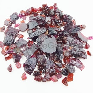 May include: A pile of rough, red and purple gemstones. The gemstones are various sizes and shapes, and some have a shiny, polished finish.
