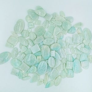 May include: A large collection of light green and white gemstone cabochons in various shapes and sizes. The stones have a shimmering, iridescent quality.