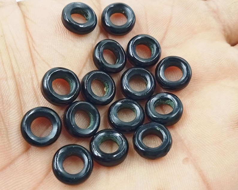 Op de afbeelding: Een verzameling zwarte ringvormige kralen met een gladde, glanzende afwerking. De kralen hebben een klein gaatje in het midden, wat suggereert dat ze bedoeld zijn voor het maken van sieraden of knutselen.