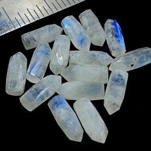 May include: A collection of 12 iridescent rainbow moonstone points, each with a unique blue flash. The points are polished and have a smooth, glassy finish.