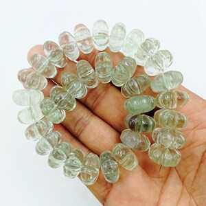 May include: A strand of light green faceted gemstone beads. The beads are oval shaped and have a carved design. The beads are strung on a wire.