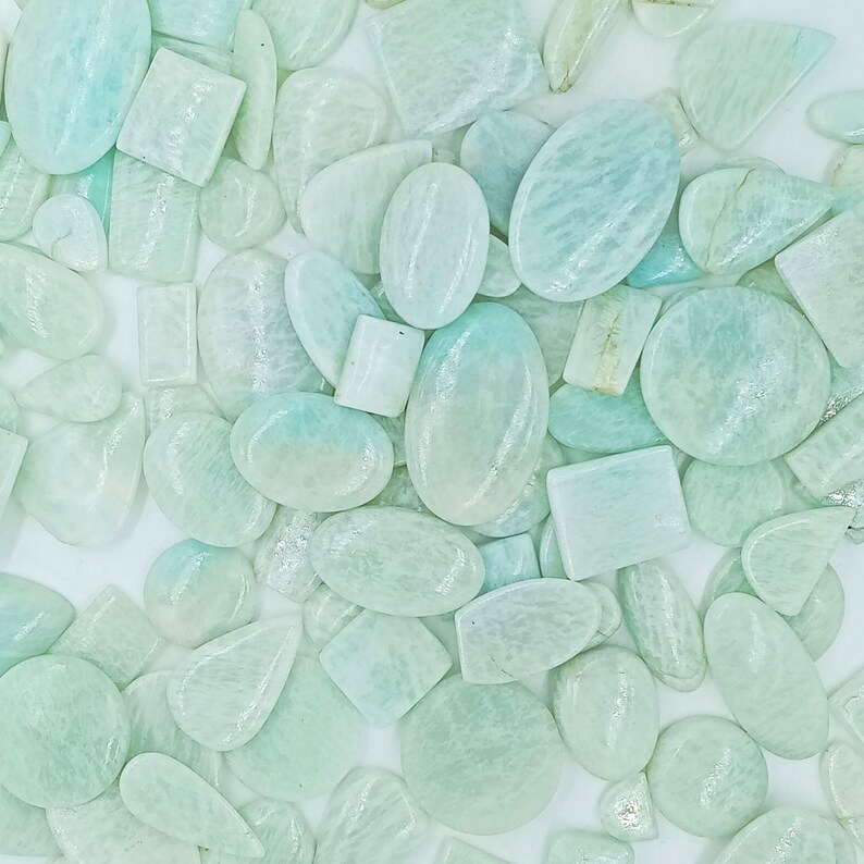 May include: A collection of light green, translucent, oval and rectangular shaped gemstones. The stones have a smooth, polished finish.