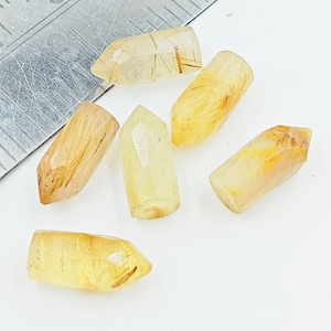 May include: Six golden rutilated quartz points, each with a unique shape and pattern of inclusions. The points are translucent and have a light yellow color.
