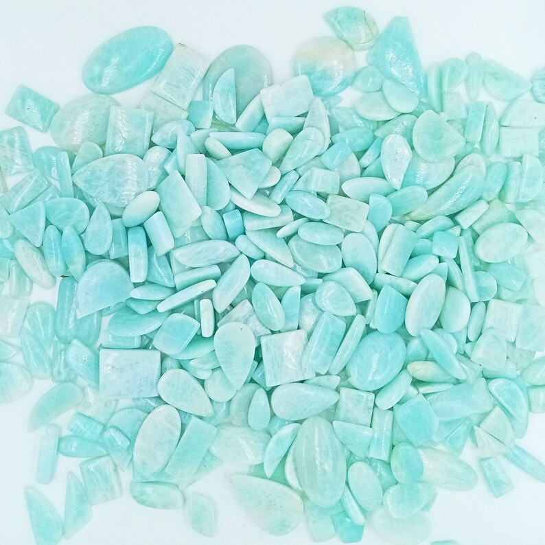 K&ouml;nnte beinhalten: Eine gro&szlig;e Sammlung von hellblauen und gr&uuml;nen Edelstein-Cabochons in verschiedenen Formen und Gr&ouml;&szlig;en. Die Cabochons sind in einem zuf&auml;lligen Muster angeordnet und bereit f&uuml;r die Verwendung in der Schmuckherstellung.