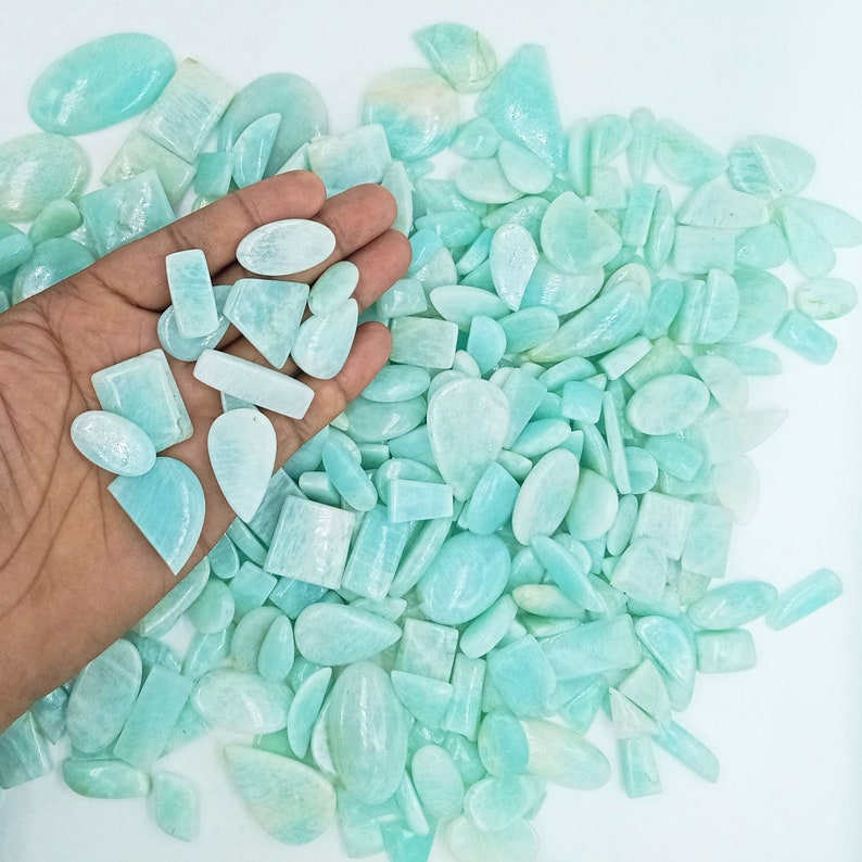 K&ouml;nnte beinhalten: Eine gro&szlig;e Sammlung von hellblauen und gr&uuml;nen Edelstein-Cabochons in verschiedenen Formen und Gr&ouml;&szlig;en. Die Cabochons sind glatt und poliert und haben ein durchscheinendes Aussehen.