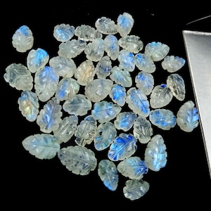Pode incluir: Uma coleção de cabochões de pedra da lua branca em forma de folha com reflexos iridescentes azuis e verdes. As pedras são esculpidas com veios de folhas detalhados e são perfeitas para a fabricação de joias.