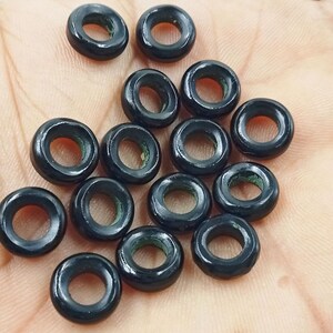 Op de afbeelding: Een verzameling zwarte ringvormige kralen met een groene binnenrand. De kralen zijn gemaakt van een glad, gepolijst materiaal en hebben een glanzende afwerking.