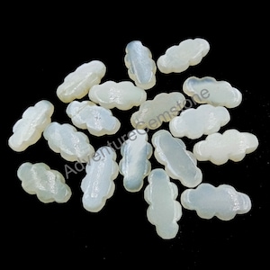 Pode incluir: Uma coleção de 15 cabochões de madrepérola branca, cada um com a forma de uma nuvem. Os cabochões são lisos e têm um brilho iridescente sutil.