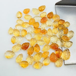 May include: A collection of approximately 50 small, carved, leaf-shaped gemstones. The gemstones are a mix of light and dark yellow.