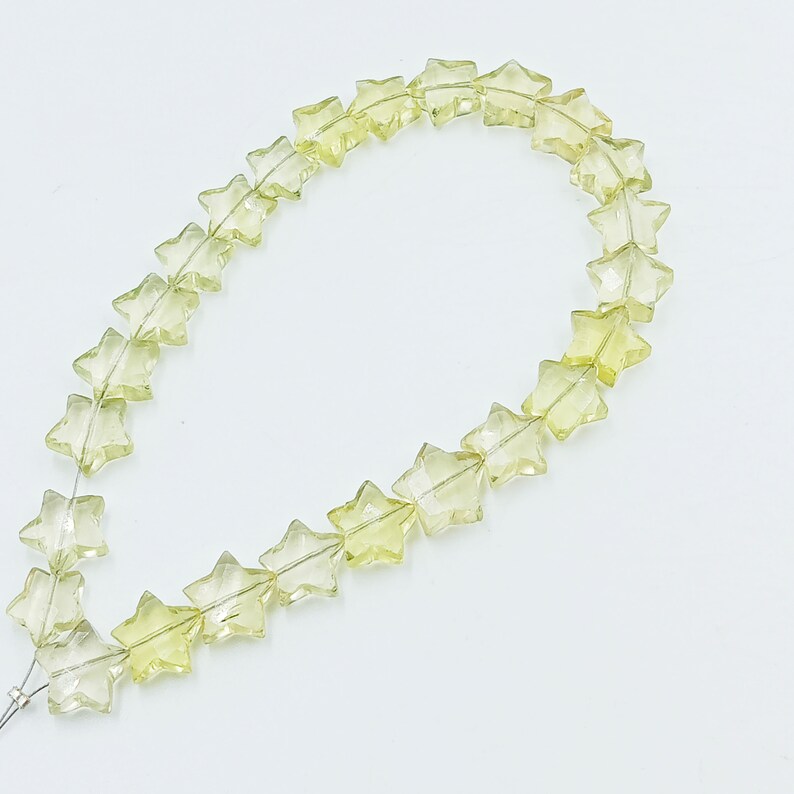 May include: A strand of light yellow star-shaped gemstone beads. The beads are faceted and have a translucent appearance.