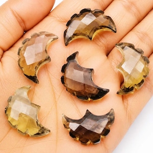 May include: Five faceted, crescent moon-shaped gemstones in varying shades of translucent brown and yellow. Each piece features a geometric, multi-faceted surface that reflects light, showcasing a polished finish and a distinct curved silhouette.