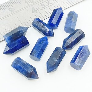 May include: Ten blue gemstone points, each with a hexagonal shape and a pointed tip. The points are arranged in a random pattern on a white surface.