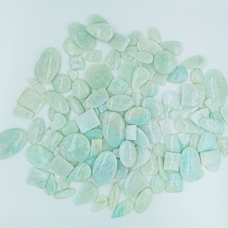 May include: A large collection of light green and white gemstone cabochons in various shapes and sizes. The stones have a shimmering, iridescent quality.