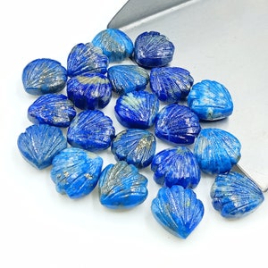 May include: A collection of blue lapis lazuli gemstone heart-shaped beads with a carved shell design. The beads are scattered on a white surface.