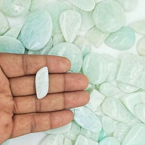 May include: A collection of light green and white amazonite cabochons of various shapes and sizes. The stones are smooth and polished, with a subtle shimmer.