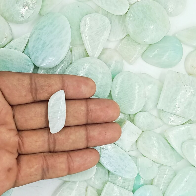 May include: A collection of light green and white amazonite cabochons of various shapes and sizes. The stones are smooth and polished, with a subtle shimmer.