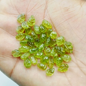 Può includere: Una collezione di perline di peridoto verde tagliate a forma di foglie. Le perline sono lisce e lucidate, con un colore verde traslucido.