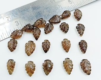 May include: A collection of 18 brown gemstone leaf shaped beads. The beads are approximately 1 inch long and are arranged on a white surface next to a ruler.