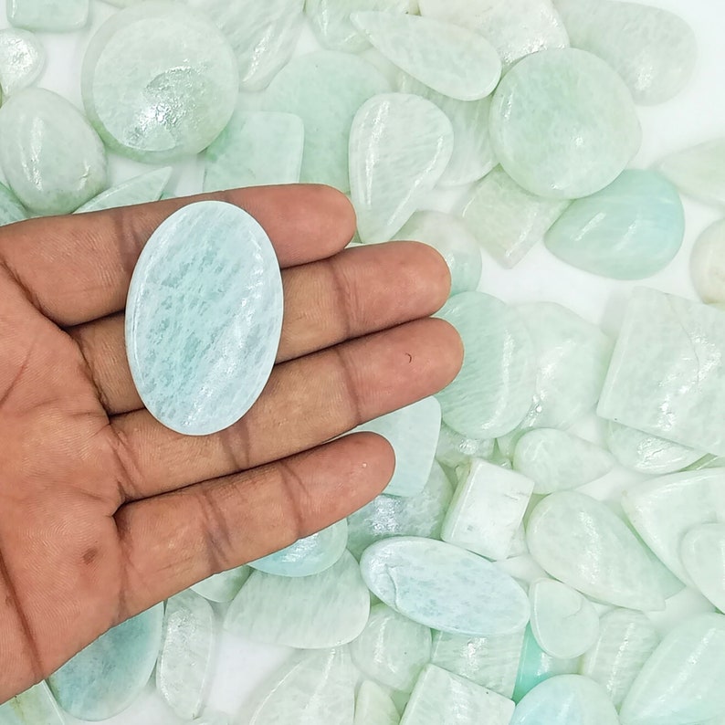 May include: A collection of smooth, light green, oval-shaped gemstones. The stones are various sizes and have a translucent appearance.