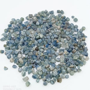 May include: A large pile of rough, blue sapphire gemstones. The stones are various sizes and shapes, with a mix of light and dark blue hues.