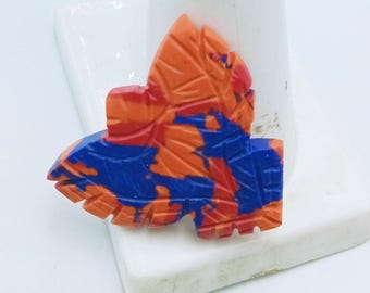 May include: A leaf-shaped decorative object with carved details. The object features a vibrant color scheme of orange, red, and blue. The leaf is displayed on a white surface.