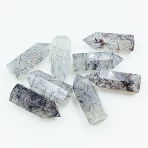 May include: A group of eight clear quartz crystal points with black and red inclusions. The points are all approximately the same size and shape, and they are arranged in a random pattern.