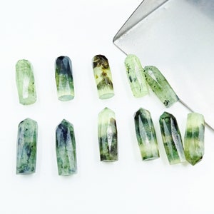 May include: A collection of ten green and black crystal points. The points are all roughly the same size and shape, and they have a smooth, polished finish.