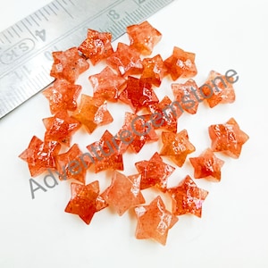 Puede incluir: Una colección de 20 piedras preciosas de piedra de sol de color naranja en forma de estrella. Las piedras miden aproximadamente 1,2 cm y tienen una textura natural y rugosa.