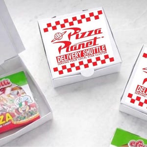May include: White pizza boxes with red checkered borders and the words "Pizza Planet Delivery Shuttle" in red. One box is open, revealing a package of pizza-shaped gummy candy.
