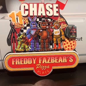 May include: A colorful cake topper featuring the name "CHASE" and the number "11". The design includes characters from the video game "Five Nights at Freddy's" and the text "FREDDY FAZBEAR'S Pizza PLACE".