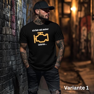 Könnte beinhalten: Schwarzes T-Shirt mit dem Text "Ich fahr mit meiner Laterne..." und einem gelben Motorsymbol. Das T-Shirt wird von einer Person getragen, die eine schwarze Kappe und dunkle Jeans trägt. Das Bild ist in einer Gasse mit Graffiti aufgenommen.