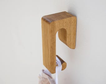 May include: A light brown wooden wall hook with a curved, J-shaped design and a visible wood grain texture. The hook is mounted to a flat surface and holds a beige fabric item by a white loop, displaying a small portion of the fabric's textured surface.