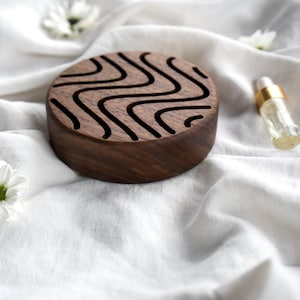 Könnte beinhalten: Ein rundes Holztablett mit einem wellenförmigen Design, das in die Oberfläche geschnitzt ist. Das Tablett ist aus dunklem Holz und hat eine natürliche Oberfläche.