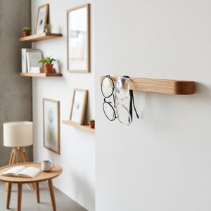 Minimalist self adhesive wooden glasses holder made from natural oak or American walnut wood, designed for modern interiors. This wall mounted reading glasses hook helps keep eyewear organized and always within reach in the office, bathroom or hallway. A practical, elegant and space saving wooden organizer with no drilling required.