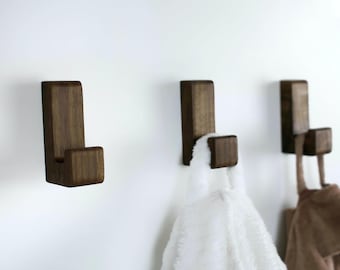 May include: Three dark brown wooden hooks mounted on a white wall. Two hooks have white and brown towels hanging from them.