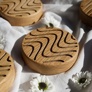 May include: Three wooden coasters featuring a wavy pattern carved into the surface. The coasters are round and made of light brown wood.