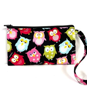 May include: A black zippered pouch with a wrist strap. The pouch is covered in a colorful owl print with pink, blue, green, and red owls on a black background.