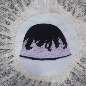 May include: A black and purple crocheted beanie hat with a flame design. The hat is made with a soft, textured yarn.