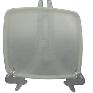 May include: A square, semi-translucent white plastic Tupperware lid with rounded corners. The center features embossed text reading Tupperware, Orlando, Florida, U.S.A., Brussels, London, Melbourne, Toronto, Tokyo, Mexico City, and 810-6.