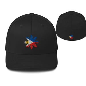 Könnte beinhalten: Schwarze Baseballkappe mit einem farbenfrohen, gestickten Design. Das Design zeigt einen Sonnenaufgang mit roten, weißen, blauen und gelben Akzenten. Die Kappe hat einen gebogenen Schirm und eine strukturierte Passform. Eine weitere Kappe ist im Hintergrund sichtbar.