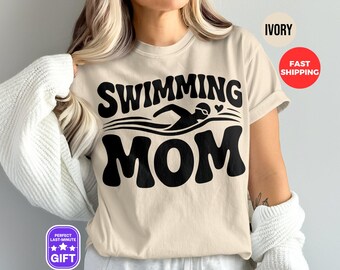 Puede incluir: Una camiseta beige con texto negro que dice "Swimming Mom" y un gráfico de un nadador. El texto está en una fuente retro.