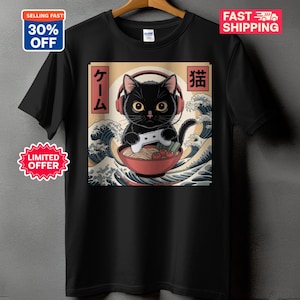 Op de afbeelding: Zwart t-shirt met een cartoonkat met een koptelefoon en een gamecontroller, in een kom ramen. Het ontwerp bevat Japanse tekst en oceaan golf graphics.