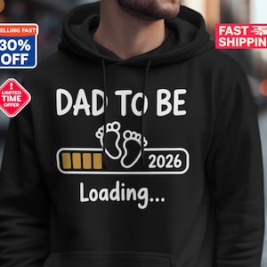 May include: Black hoodie with the text "DAD TO BE" in white, baby footprints, and the year "2026". The word "Loading..." is also displayed. The hoodie has a drawstring hood.