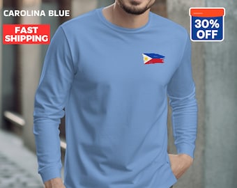 May include: A light blue long-sleeved t-shirt with a faded, brushstroke design of the Philippine flag on the left chest. "CAROLINA BLUE" and "FAST SHIPPING" are written in red text at the top of the image.