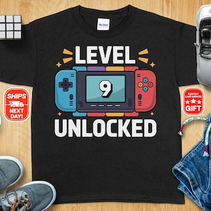Peut inclure: T-shirt noir avec un graphique blanc d'une manette de jeu vidéo avec le texte "Niveau 9 Débloqué".