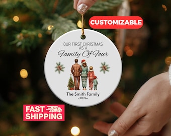May include: A white ceramic Christmas ornament with a family portrait and the text "OUR FIRST CHRISTMAS AS A Family Of Four". The ornament features a family of four, a Christmas tree, and the family name and year.