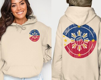 May include: A beige hoodie with a distressed, circular design featuring the Philippine flag with a raised fist in the center. The flag is red, white, and blue with a yellow sun and stars.