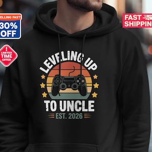 Può includere: Felpa con cappuccio nera con la scritta "LEVELING UP TO UNCLE EST. 2026", un design retrò a tramonto e un controller per videogiochi. La felpa ha un cappuccio con coulisse e una tasca frontale.