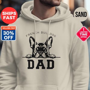 以下が含まれることがあります： フレンチブルドッグの黒いグラフィックと「DAD」の文字がプリントされたサンドカラーのパーカー。犬の上には「FRENCH BULLDOG」の文字。パーカーにはフードとフロントポケットが付いています。